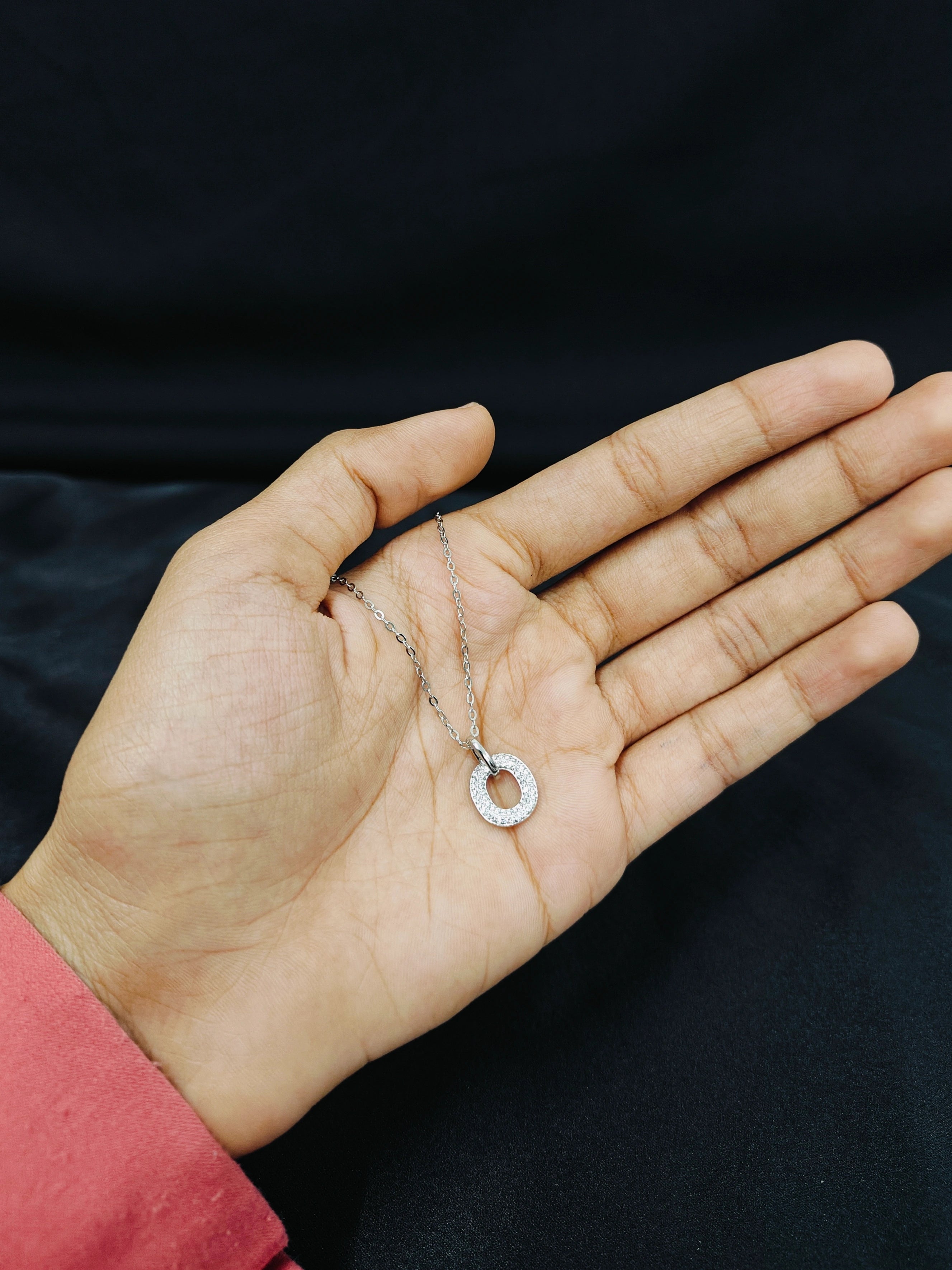 Hand holding a silver necklace with a circular pendant against a dark background